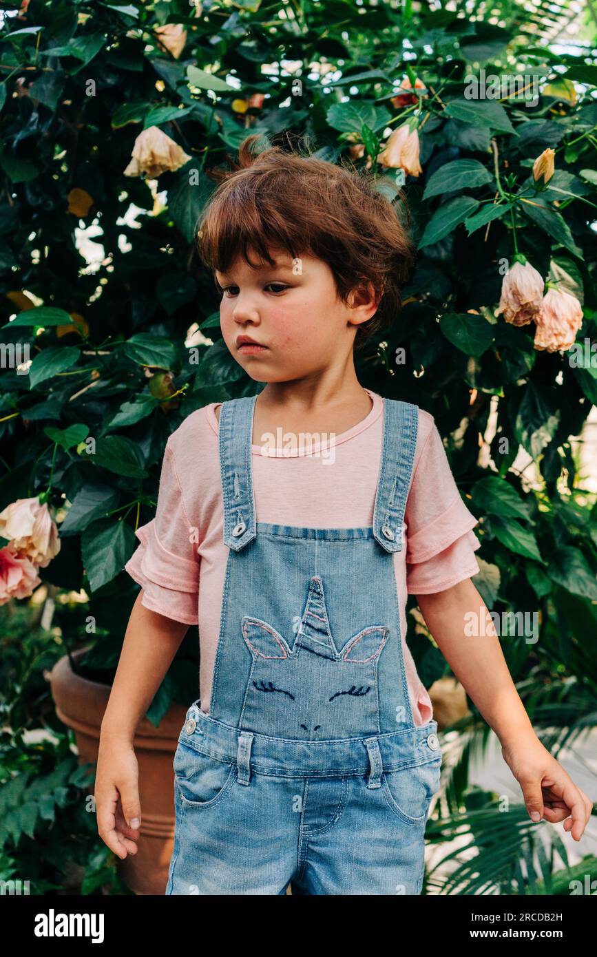 Bambina in piedi accanto alla pianta di fiori Foto Stock