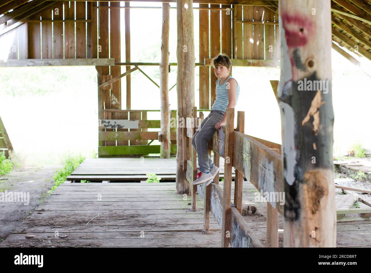 Sad Boy in Striped Shirt siede da solo nell'edificio abbandonato Foto Stock