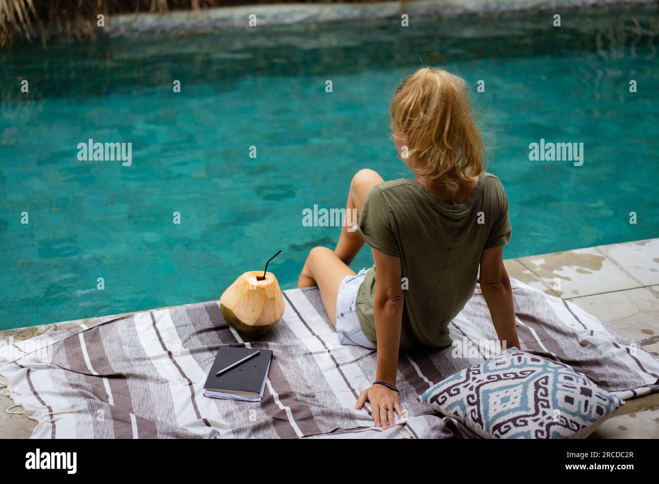 Una giovane donna passa del tempo vicino alla piscina, scrivendo un diario. Foto Stock
