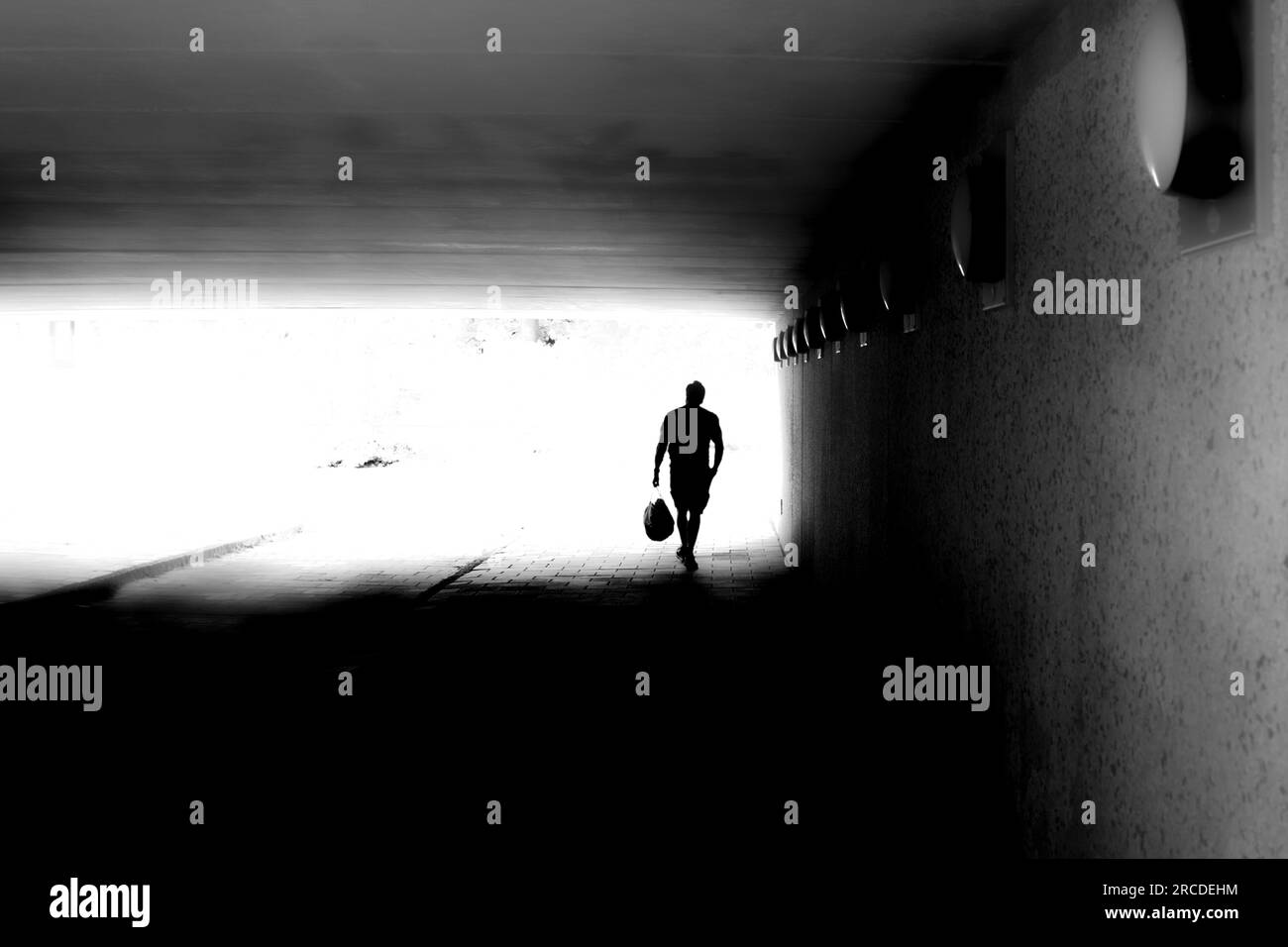 Silhouette di un uomo irriconoscibile in movimento sfocato che cammina in un tunnel buio Foto Stock
