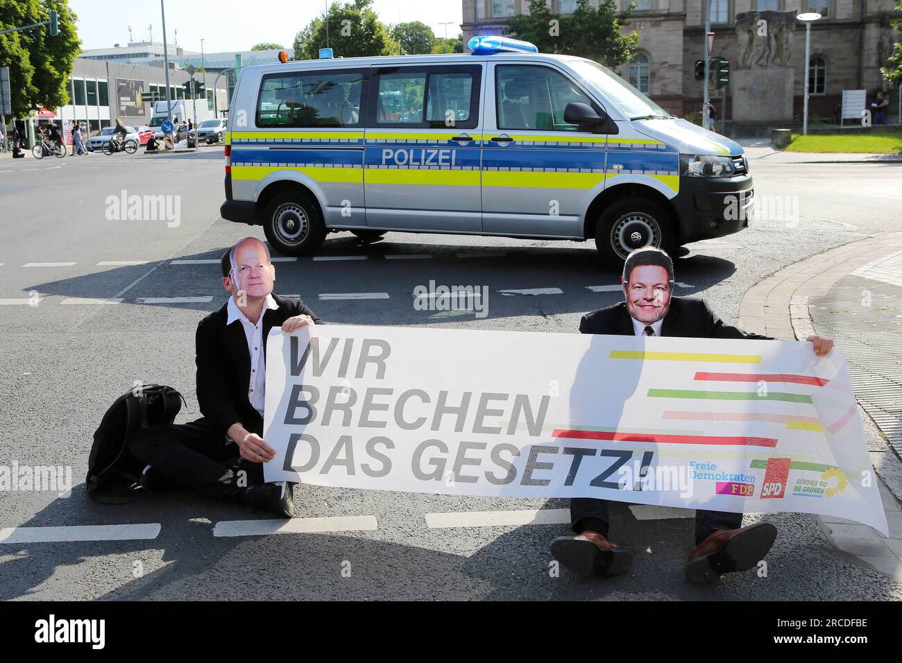 14 luglio 2023, bassa Sassonia, Göttingen: Gli attivisti del clima del gruppo Letzte Generation siedono con le maschere del Cancelliere Scholz (l) e del Ministro dell'economia Habeck durante un sit-in in un incrocio di fronte a un'auto della polizia. Gli attivisti tengono uno striscione con la scritta "stiamo violando la legge!” Foto: Stefan Rampfel/dpa Foto Stock 14 luglio 2023, bassa Sassonia, Göttingen: Gli attivisti del clima del gruppo Letzte Generation siedono con le maschere del Cancelliere Scholz (l) e del Ministro dell'economia Habeck durante un sit-in in un incrocio di fronte a un'auto della polizia. Gli attivisti tengono uno striscione con la scritta "stiamo violando la legge!” Foto: Stefan Rampfel/dpa Foto Stock
