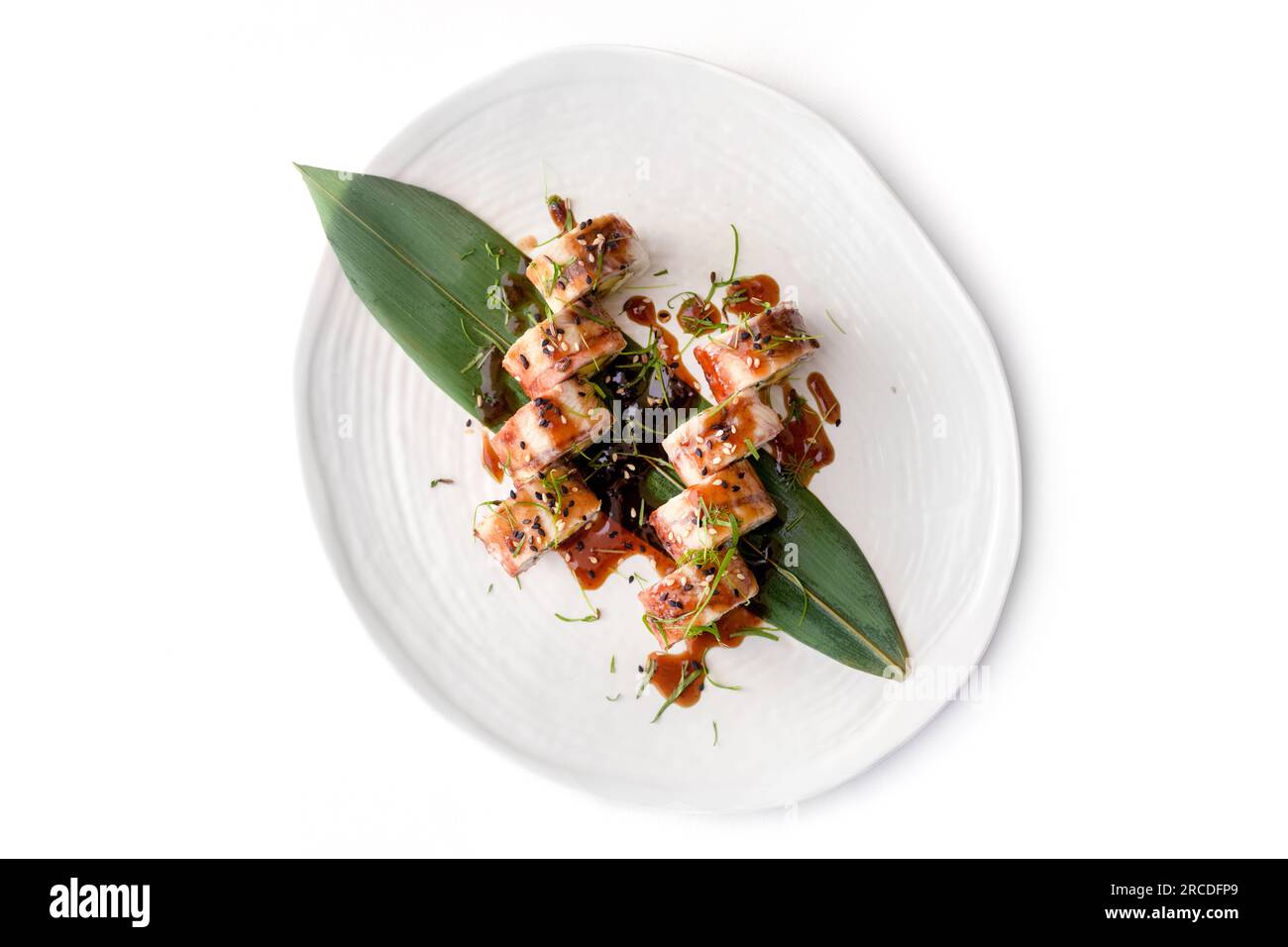 Sushi roll con cucina asiatica moderna con anguilla su piatto bianco su sfondo bianco di cemento Foto Stock