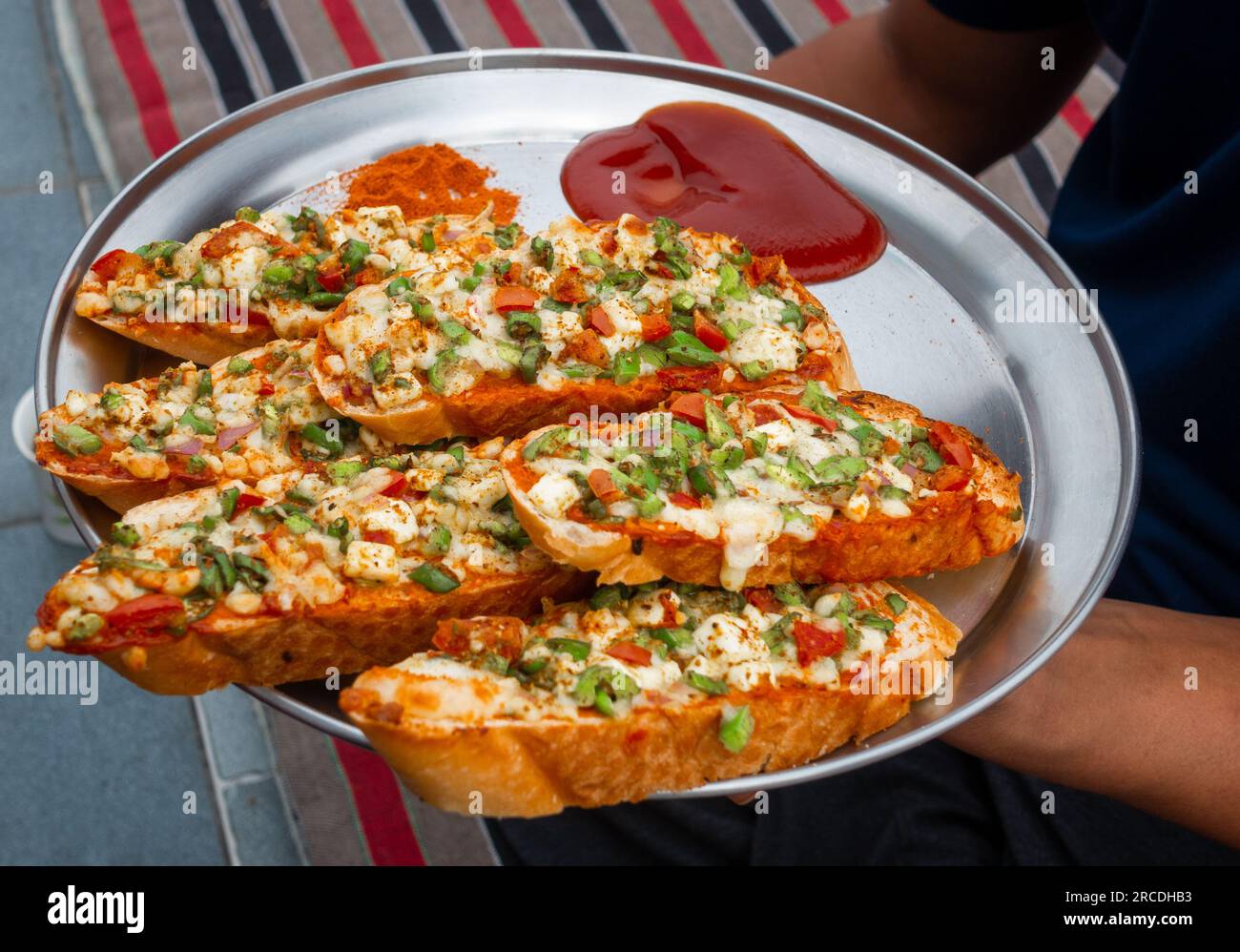Mani che tengono in mano il pane all'aglio allo zenzero fatto in casa con formaggio e condimenti alle erbe indiane. India Foto Stock