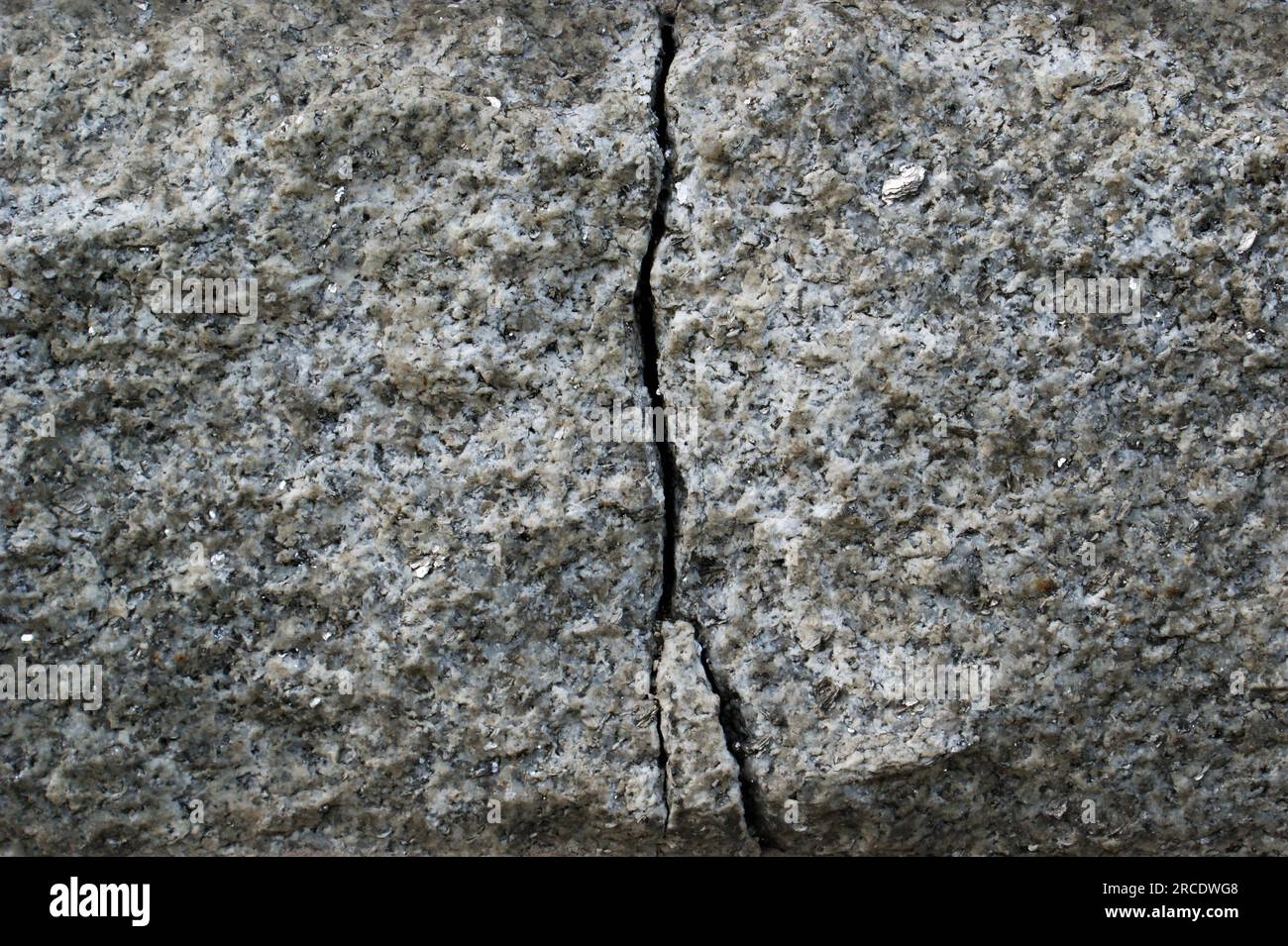 Grosse crepe nel blocco di granito. Primo piano del muro di pietra incrinato. Foto Stock