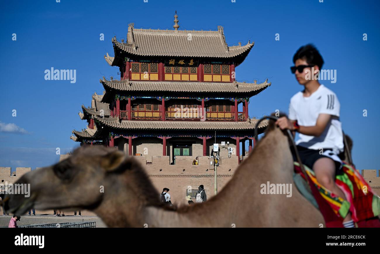 Jiayuguan, provincia cinese del Gansu. 13 luglio 2023. Un turista cavalca un cammello al passo Jiayu nella città di Jiayuguan, provincia del Gansu della Cina nord-occidentale, 13 luglio 2023. Il passo Jiayu, una famosa parte della grande Muraglia costruita durante la Dinastia Ming (1368-1644), ha attirato molti visitatori durante la stagione turistica estiva. Crediti: Liu Jinhai/Xinhua/Alamy Live News Foto Stock