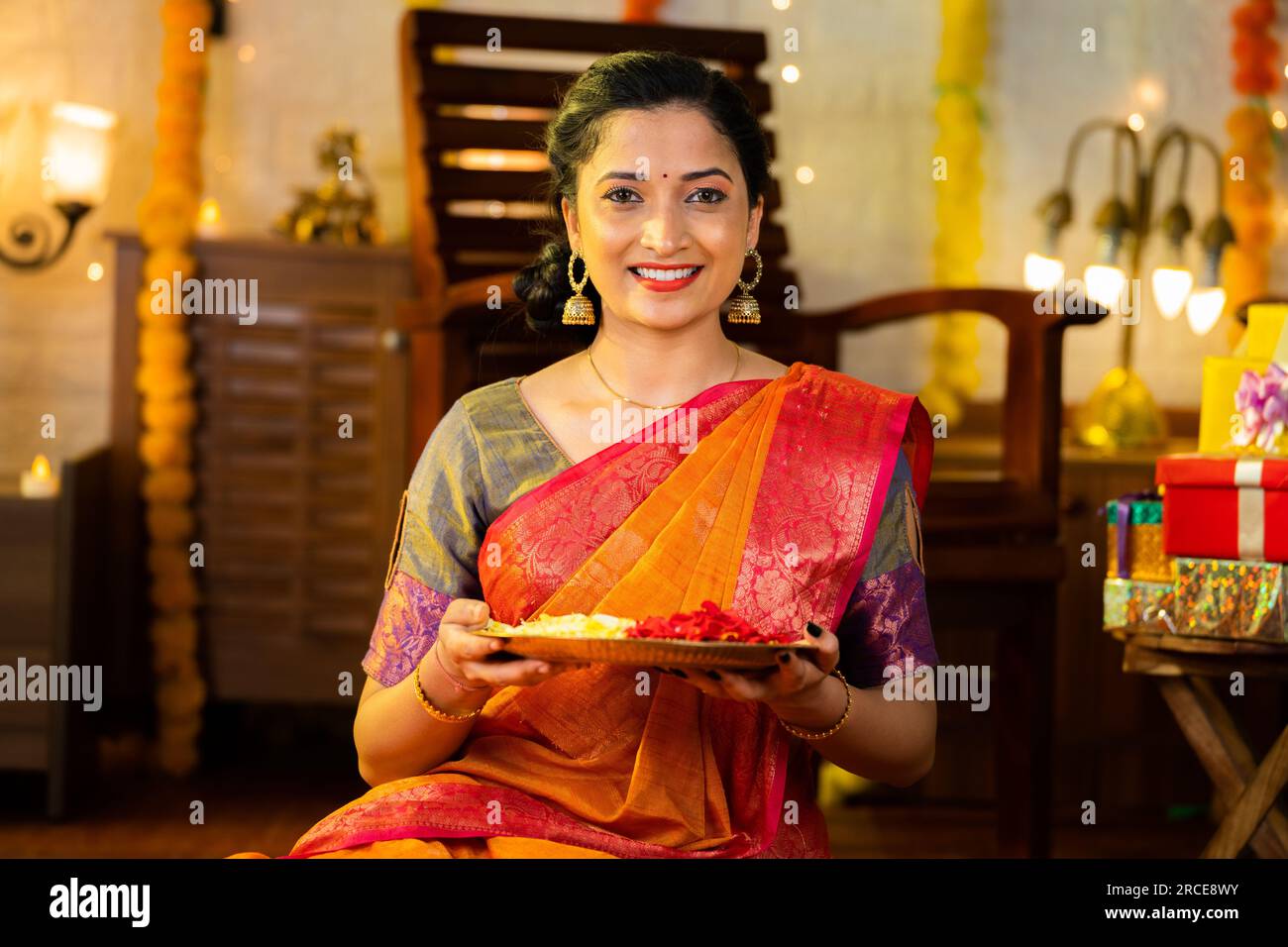 Ragazza sorridente indiana che tiene un piatto di fiori per la celebrazione diwali osservando il concetto di casa propria di tradizione indiana, cerimonia e. Foto Stock