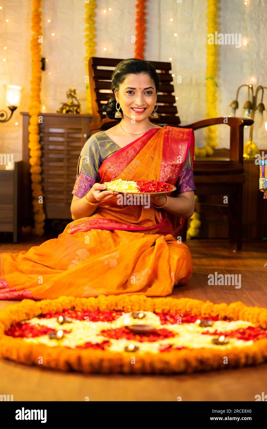 Scatto Vertcial di una ragazza indiana felice che tiene un piatto di fiori per la celebrazione diwali guardando la macchina fotografica a casa - concetto di tradizionale indiana, cerimonia Foto Stock