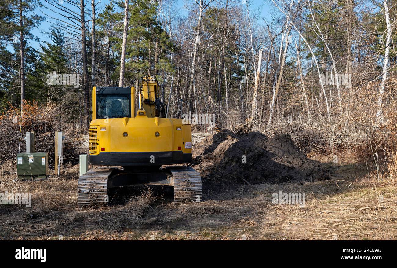 L'escavatore idraulico giallo retroescavatore con cingoli è parcheggiato in prossimità di cassette di servizio in cantiere, con alberi in lontananza. Foto Stock