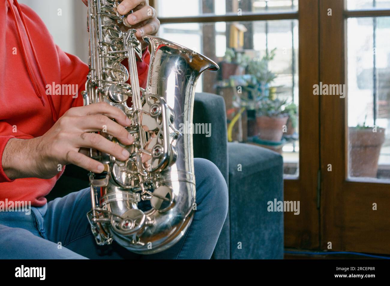 primo piano di profilo con spazio copia di mani maschili caucasiche di un uomo irriconoscibile seduto sul divano che suona un sassofono all'interno di casa. Foto Stock