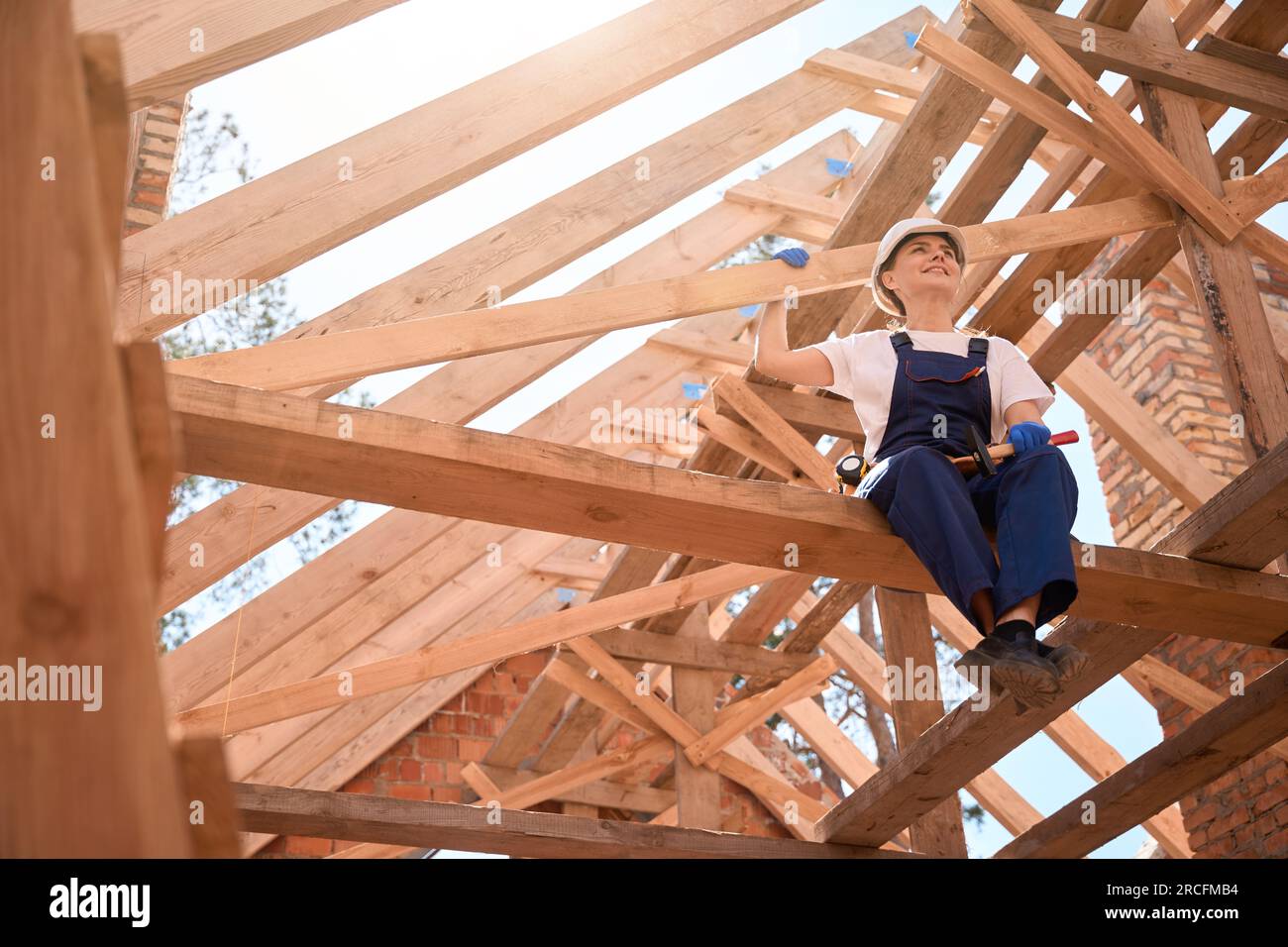 Donna che tiene il martello, che riposa dal soffitto, seduta sulla trave del tetto Foto Stock
