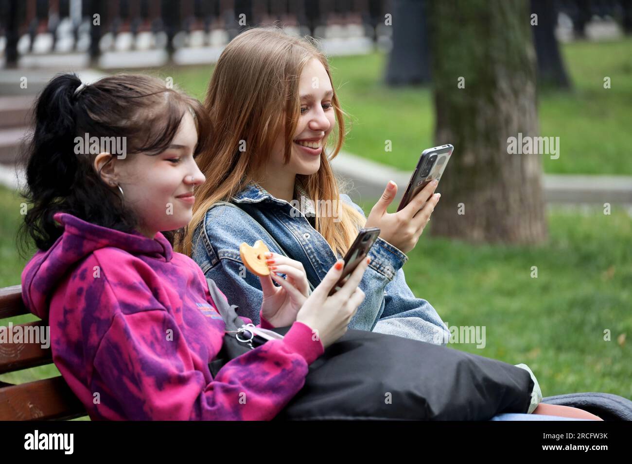 Due ragazze felici sedute in strada e che usano smartphone. Ragazze con telefoni cellulari in città estive Foto Stock