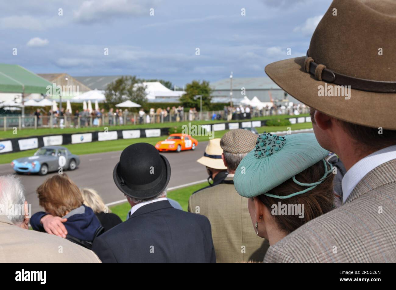 Persone in abbigliamento vintage che guardano le corse automobilistiche vintage al Goodwood Revival. Auto da corsa classiche. Un'attrazione turistica senza tempo Foto Stock