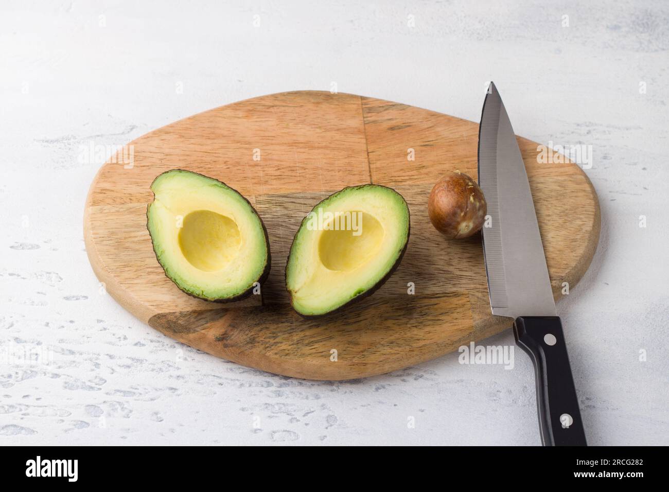 Avocado fresco tagliato a metà e fossa di avocado con un coltello su una tavola di legno su sfondo grigio chiaro, vista dall'alto. Foto Stock