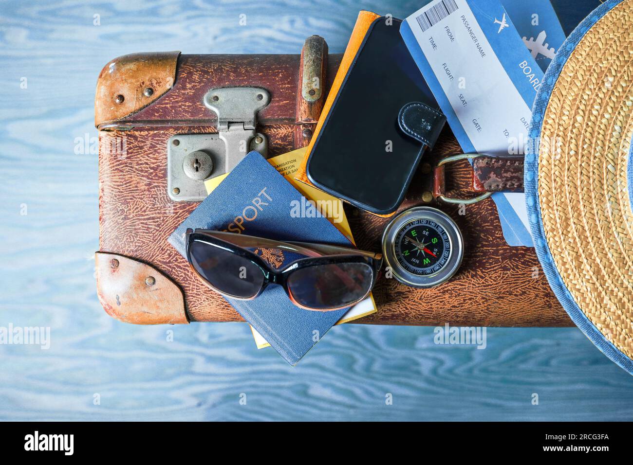 Accessori di viaggio come passaporto, biglietto d'imbarco, occhiali da sole, telefono cellulare e bussola su una valigia vintage, sfondo in legno blu ondulato, vista dall'alto f Foto Stock