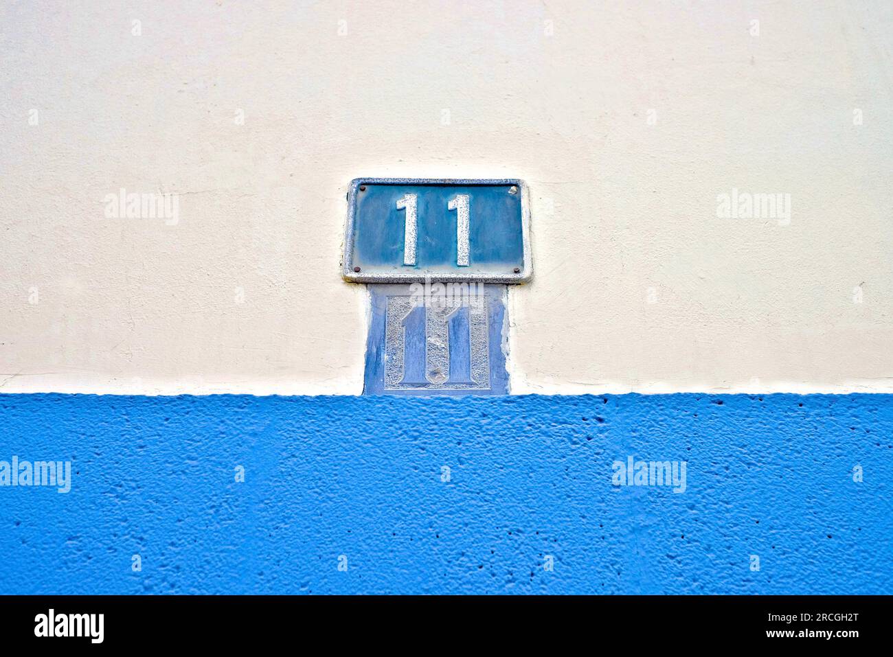Numero 11, undici, piatto blu su parete pallida e grigia. Foto Stock