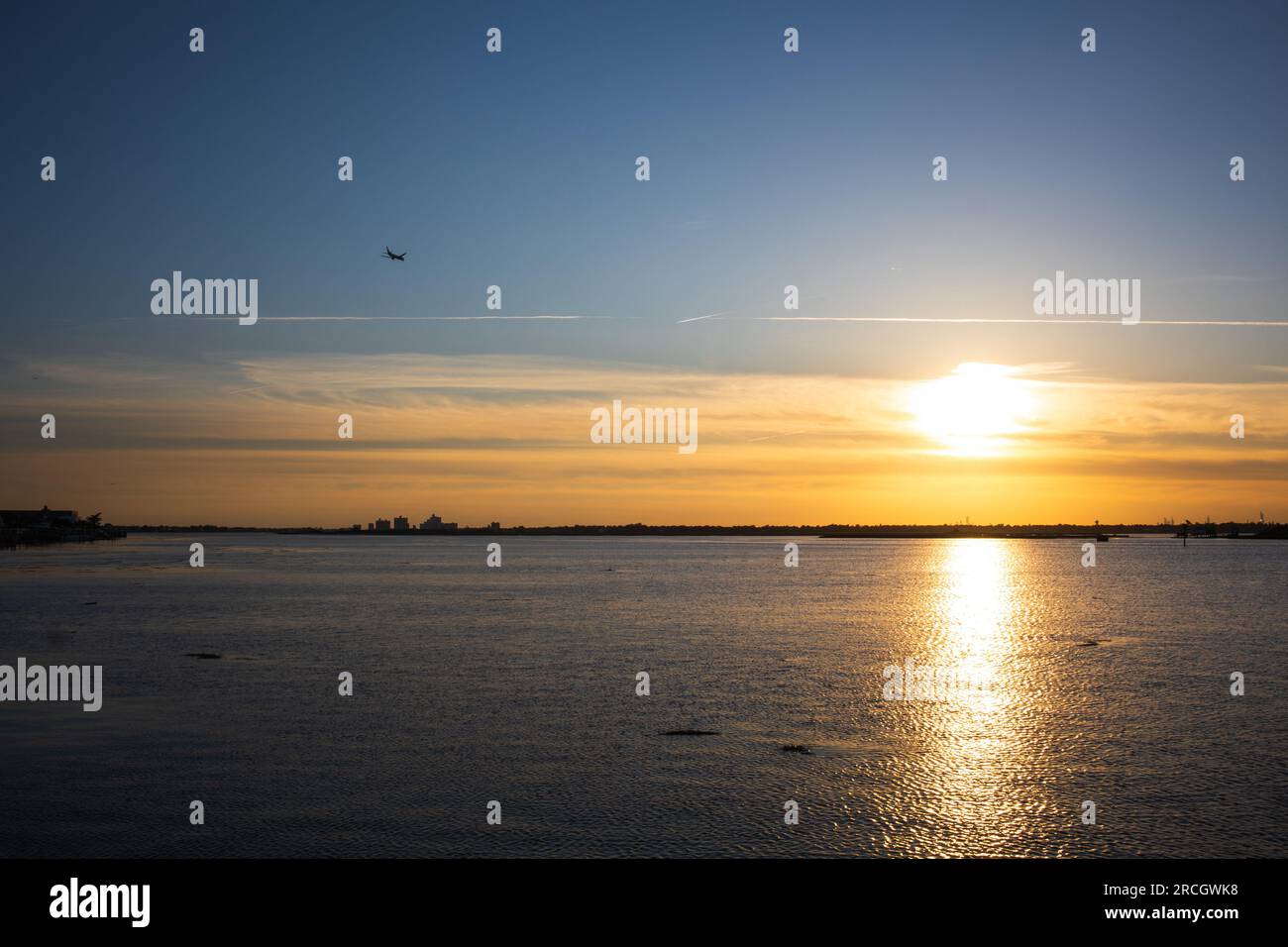 Paesaggio che raffigura il sole che tramonta a Long Island, New York, con le unghie nel cielo, gli alberi sullo sfondo e il riflesso dell'oceano. Foto Stock
