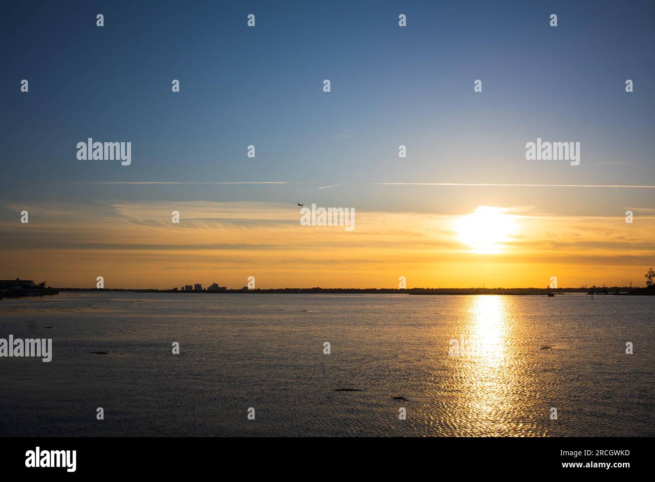 Paesaggio che raffigura il sole che tramonta a Long Island, New York, con le unghie nel cielo, gli alberi sullo sfondo e il riflesso dell'oceano. Foto Stock