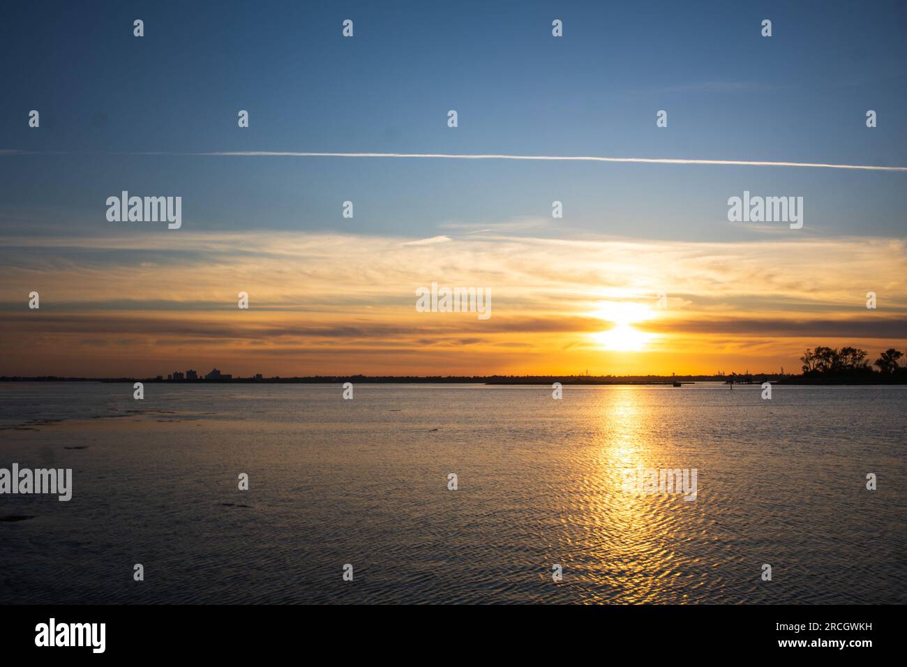 Paesaggio che raffigura il sole che tramonta a Long Island, New York, con le unghie nel cielo, gli alberi sullo sfondo e il riflesso dell'oceano. Foto Stock