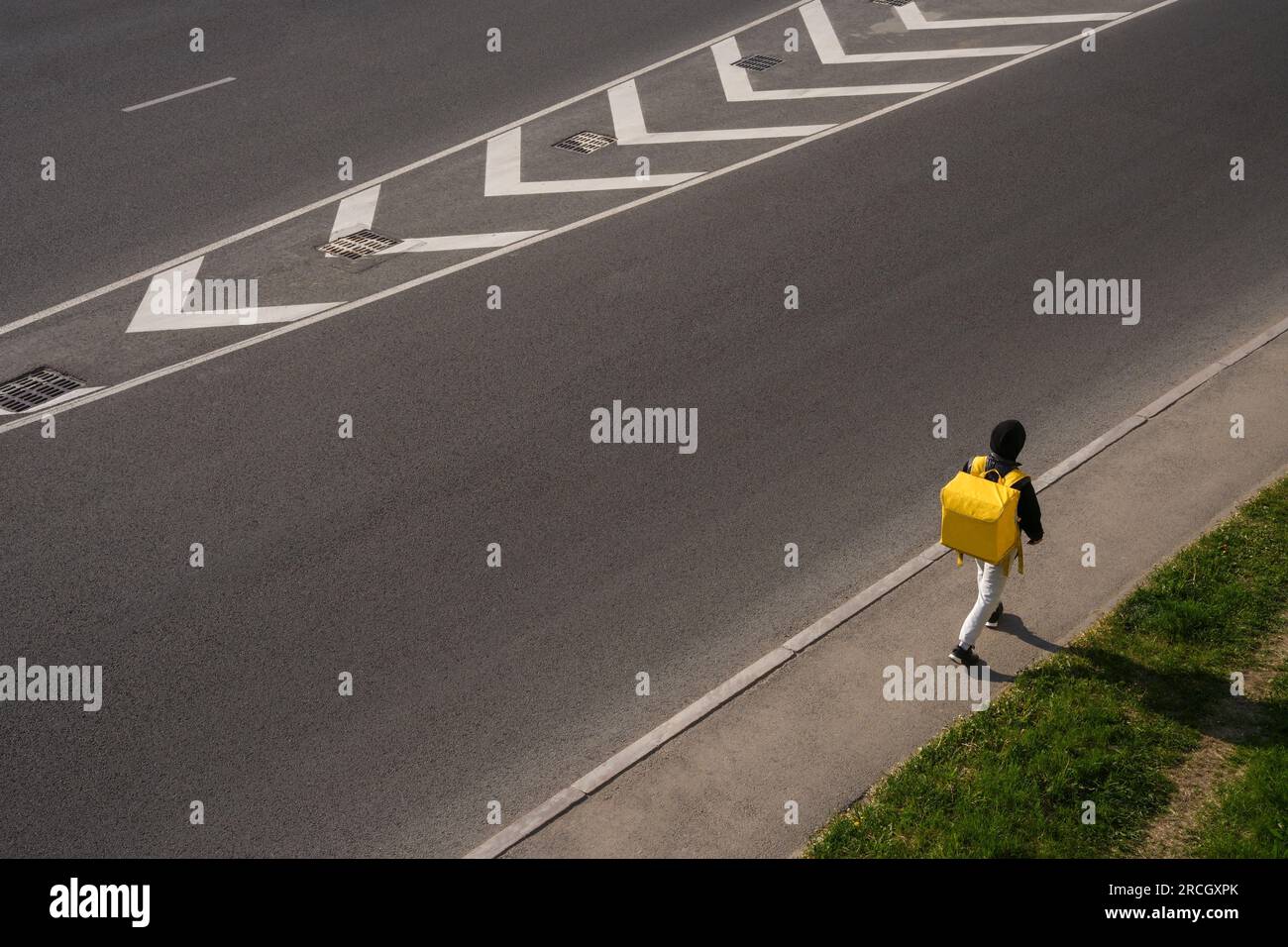 Un uomo cammina lungo il marciapiede vicino alla strada con una borsa per la consegna gialla. Foto Stock