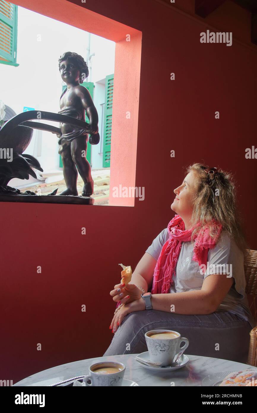 Nella foto, una ragazza che fa colazione in un bar. Esamina con interesse la statua che mostra il ragazzo. Foto Stock