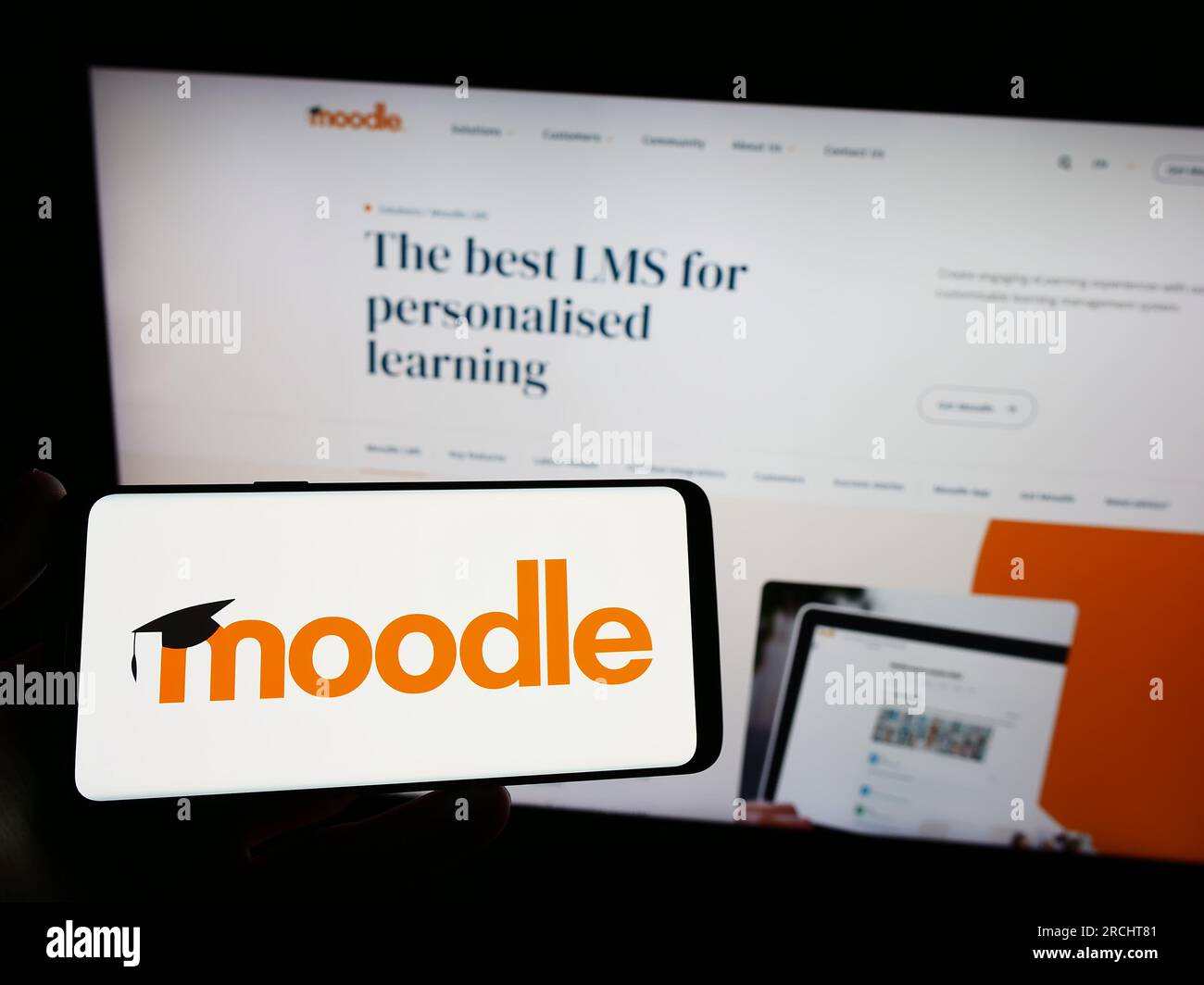 Persona che possiede uno smartphone con il logo della piattaforma di apprendimento Moodle sullo schermo di fronte al sito Web. Concentrarsi sul display del telefono. Foto Stock