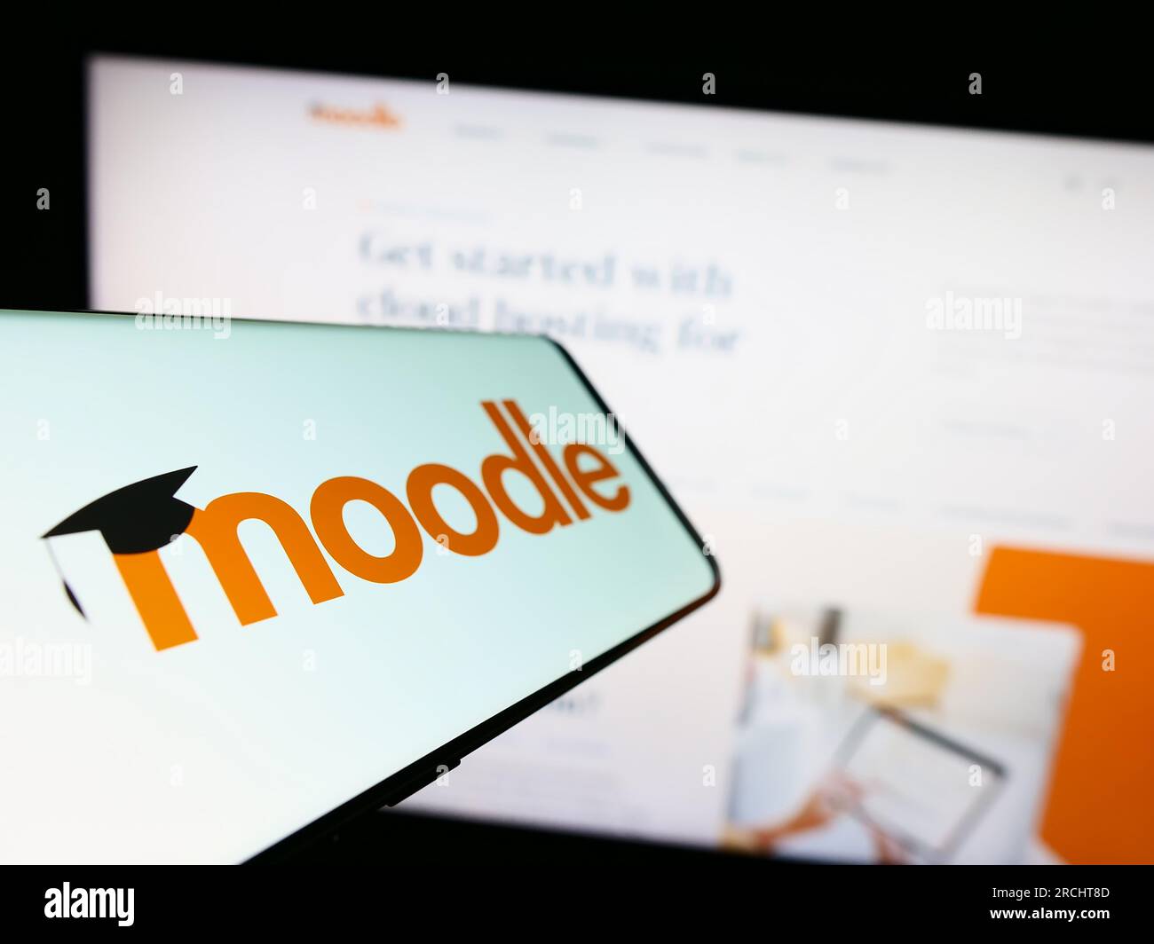 Telefono cellulare con logo della piattaforma di apprendimento Moodle sullo schermo di fronte al sito Web. Mettere a fuoco il display centrale sinistro del telefono. Foto Stock