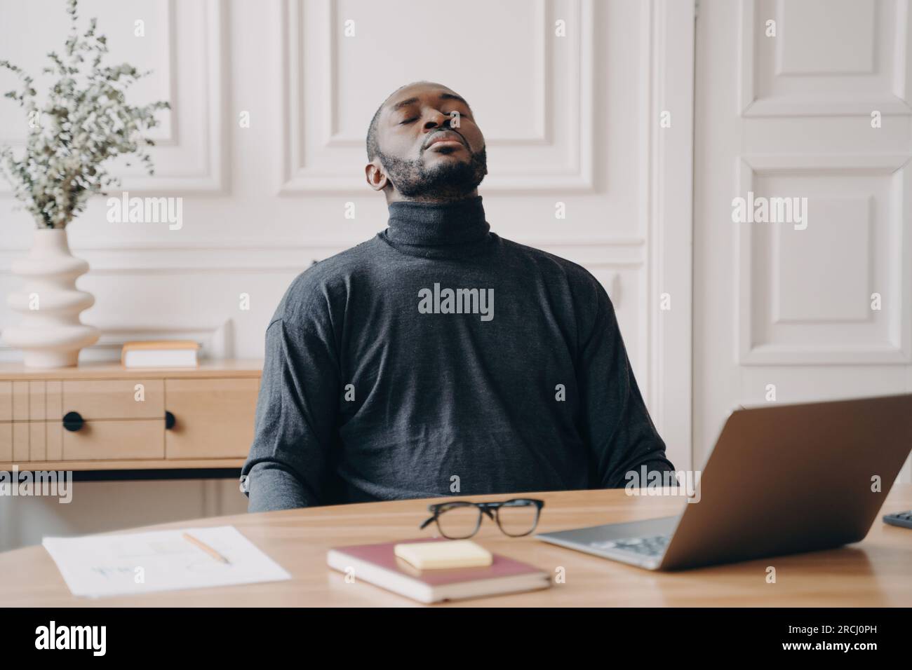 Un dipendente afro americano stanco riposa, rimuove gli occhiali, chiude gli occhi e si inclina all'indietro, recuperando dal lavoro remoto. Foto Stock