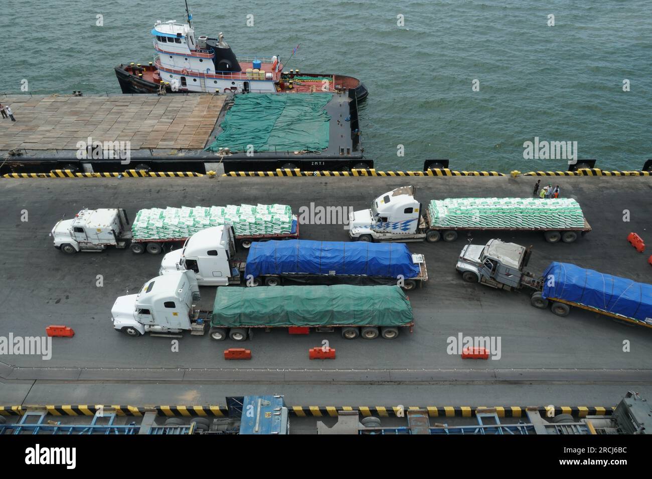 Carrelli a pieno carico con sacchetti di fertilizzante che si avvicinano al molo per lo scarico manuale da parte dei stevedores. Foto Stock