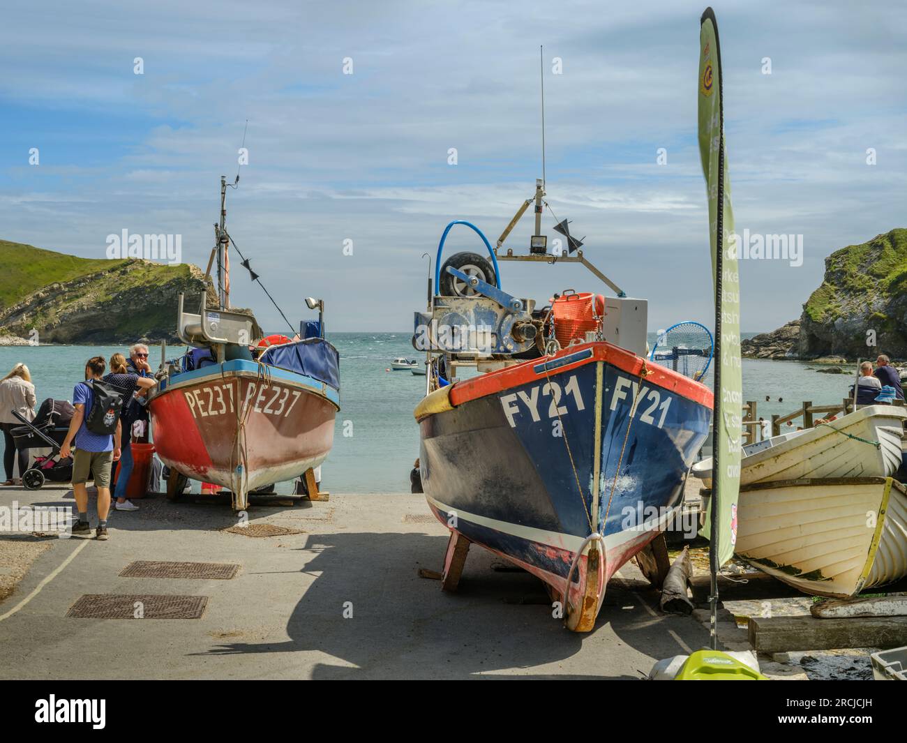 In un giorno d'estate, le piccole barche da pesca che fiancheggiano lo scalo di Lulworth Cove nel Dorset si rivelano un'attitudine popolare per i turisti. Foto Stock