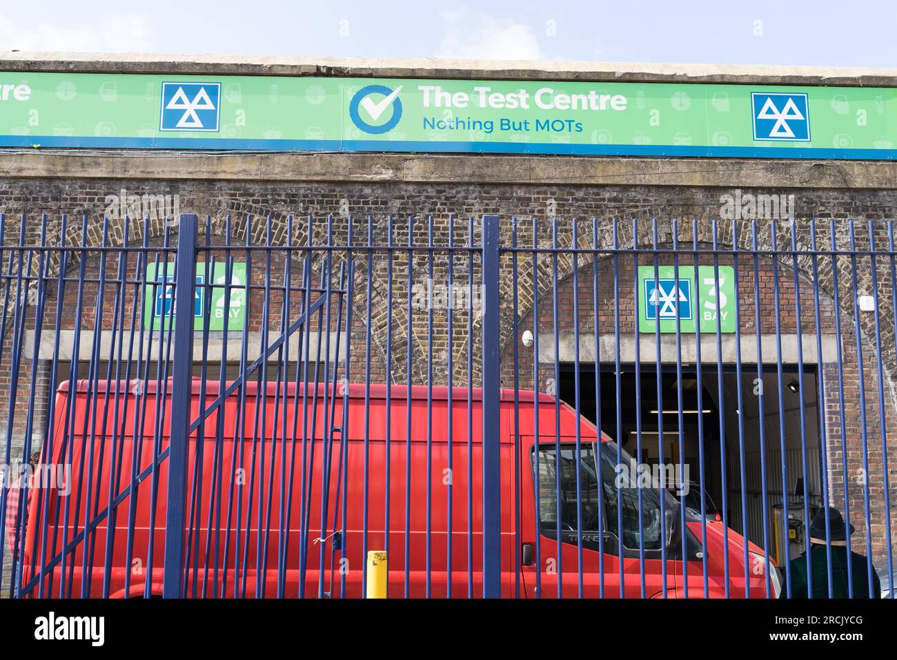 Un uomo con un cappello da lanciatore nero che si trova sulla recinzione accanto a un furgone rosso fuori dalla stazione di prova della mot in attesa di essere servito Londra Inghilterra Regno Unito Foto Stock