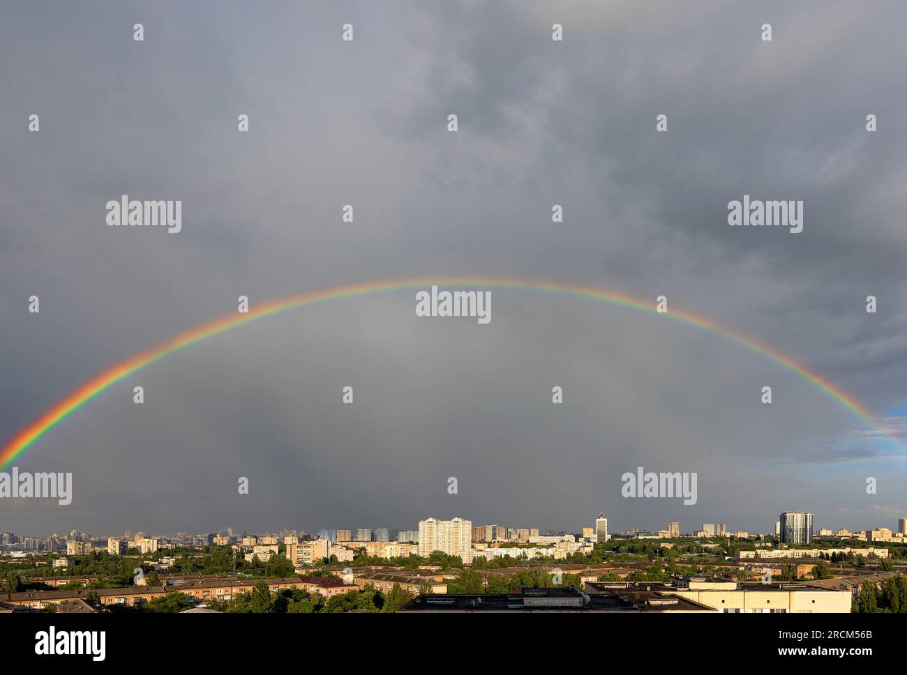 Un arcobaleno colorato nel paesaggio urbano sopra i tetti delle case cittadine contro un cielo grigio e al sole. Copia spazio. Foto Stock