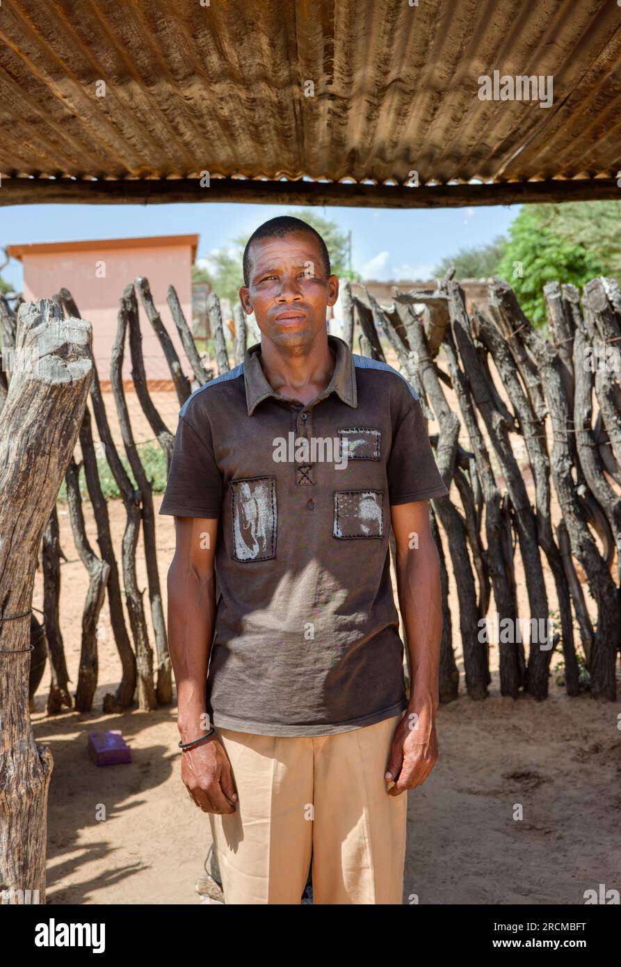 uomo africano del villaggio in piedi sotto il capannone di metallo di fronte a una recinzione di legno Foto Stock