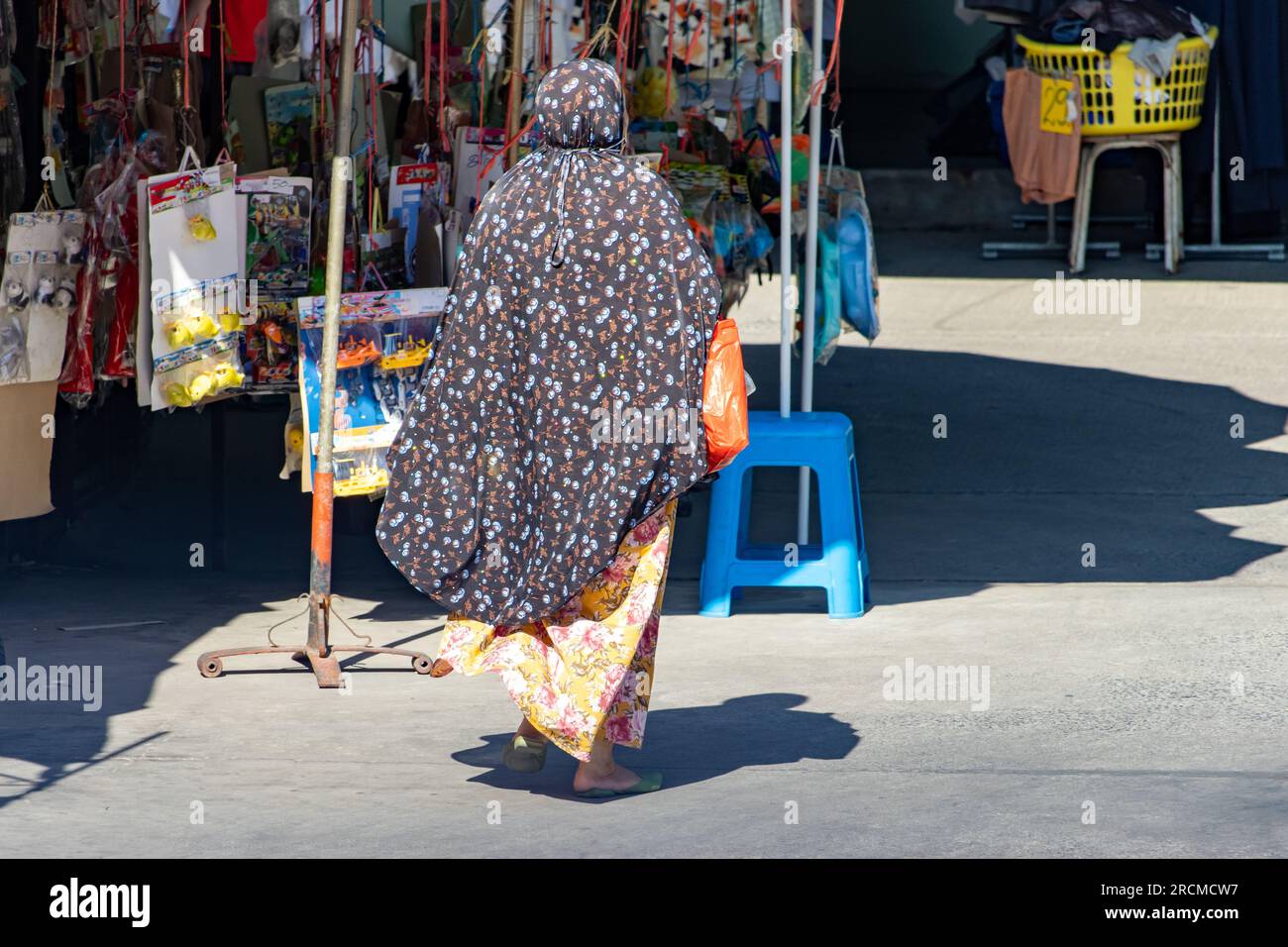 Una donna velata cammina lungo la strada con chioschi, Thailandia Foto Stock