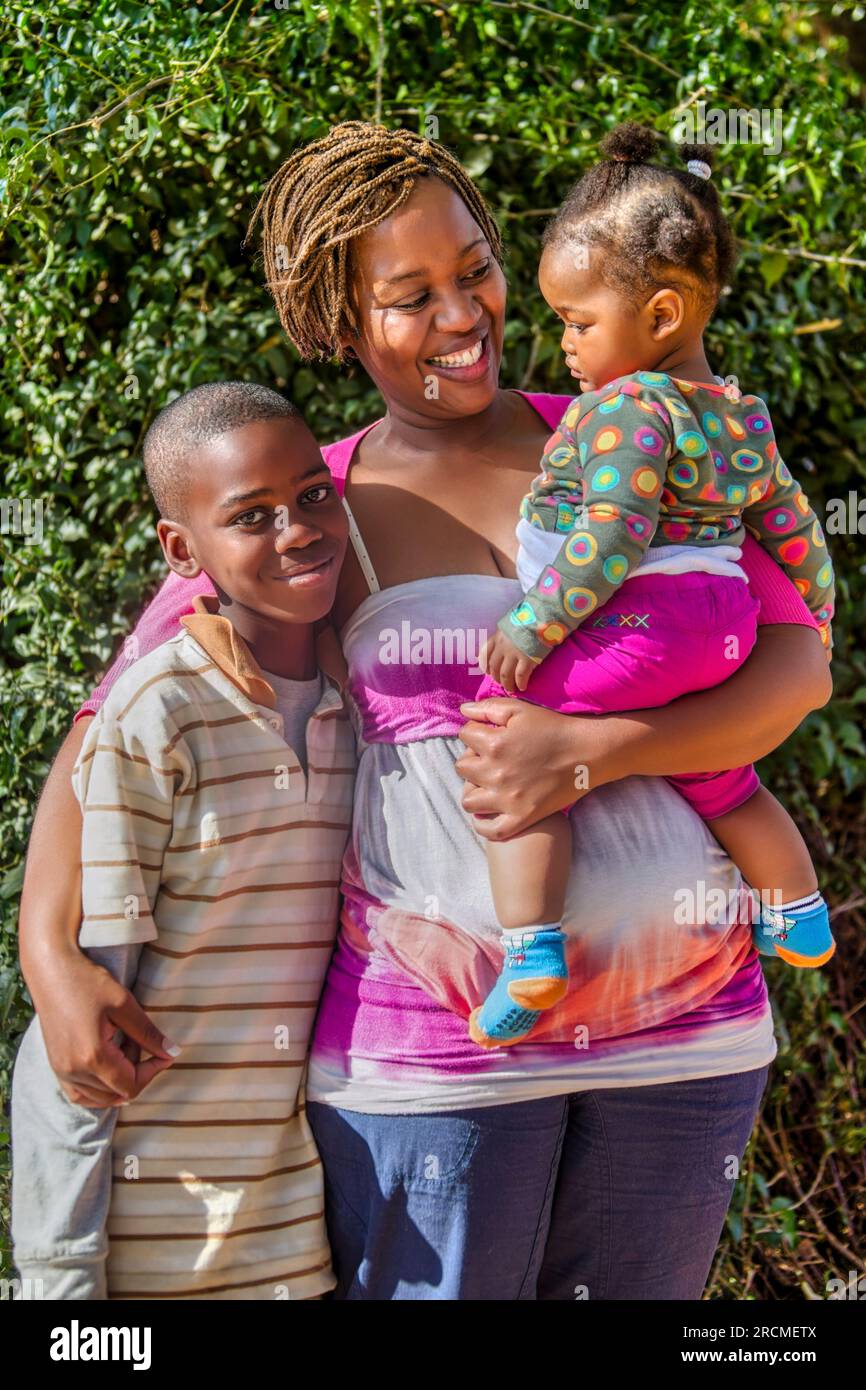 Ritratto di una famiglia africana con una madre single che abbraccia e tiene in braccio i suoi due figli Foto Stock