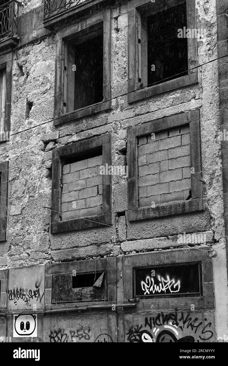 Finestre in mattoni e graffiti su un edificio vuoto abbandonato nel centro di Porto, degrado urbano su bianco e nero Foto Stock