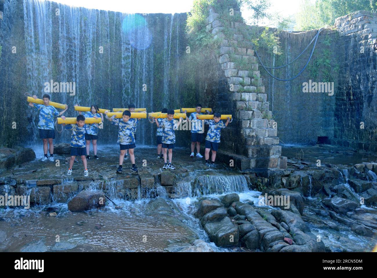 ZAOZHUANG, CINA - 16 LUGLIO 2023 - i bambini si allenano con lo squat di fronte a una cascata presso la Happiness Bay Extended Training base in X Foto Stock