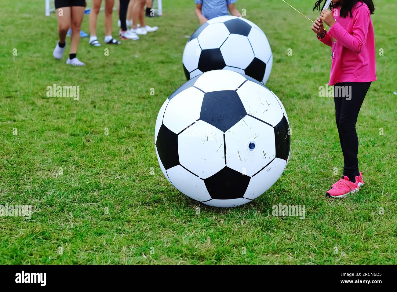 Bambini che giocano a una gigantesca palla da calcio su un campo verde. Attività divertenti per bambini e sfondo per eventi all'aperto. Foto Stock