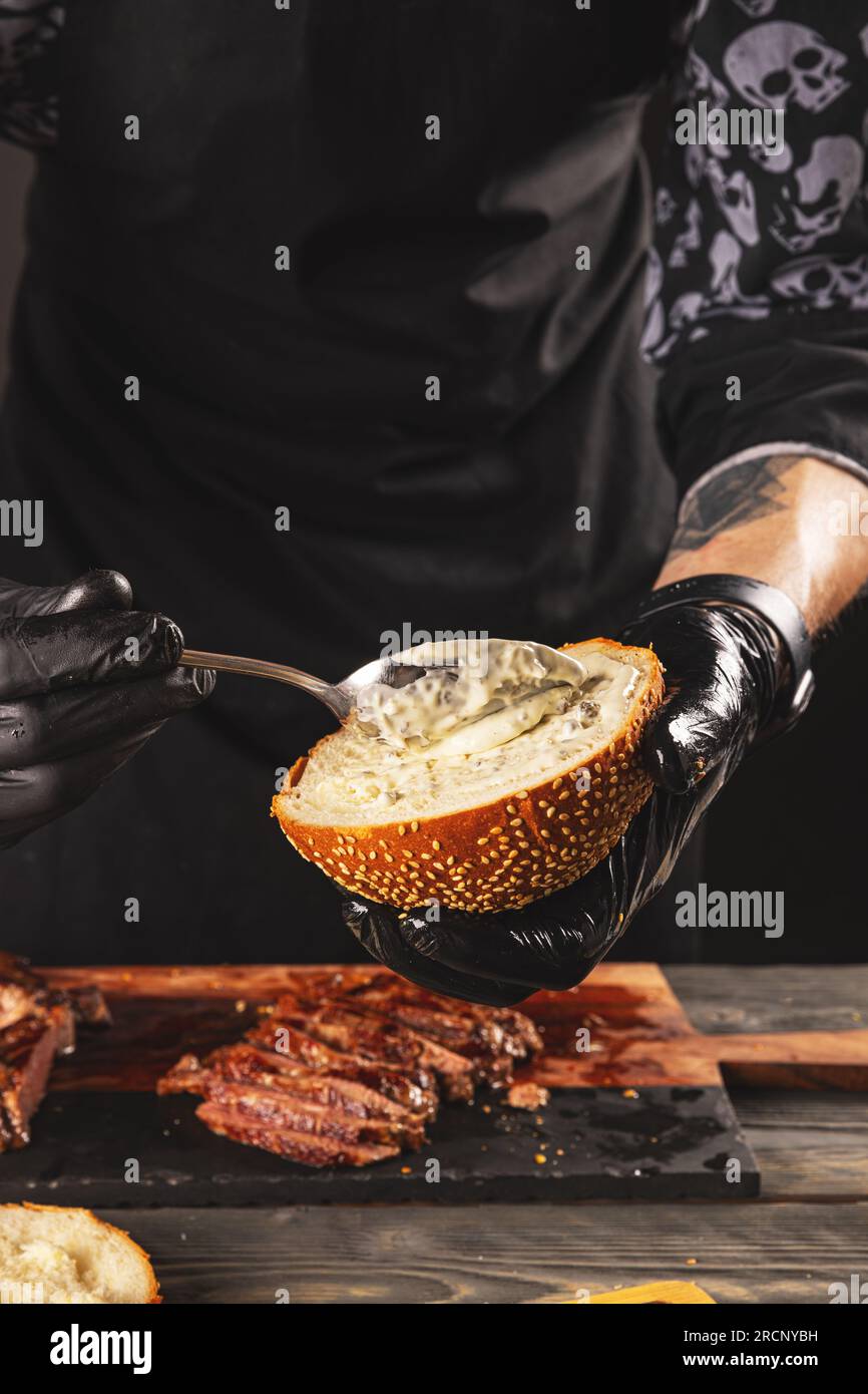 Cuocere preparando l'hamburger di bistecca aggiungendo la salsa. Il processo di fare un hamburger. Foto Stock