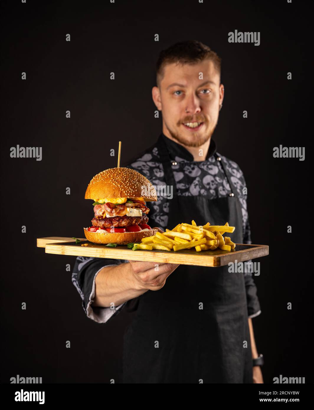 Un maestro chef sorridente in uniforme che guarda la macchina fotografica, tenendo il piatto con hamburger servito. Foto Stock