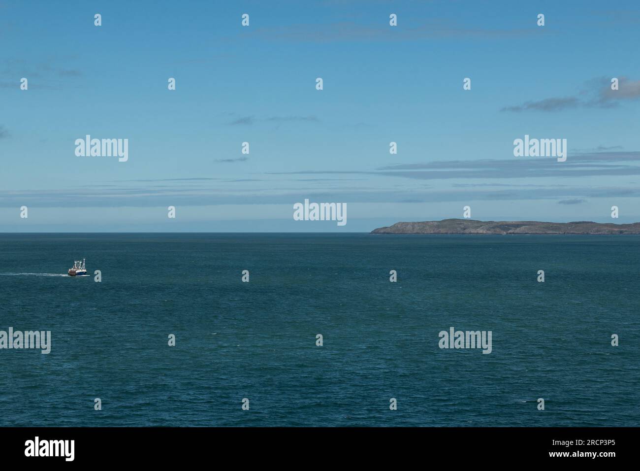 Barca da pesca solitaria su un mare blu calmo con una terra lontana all'orizzonte sotto un cielo limpido, Mare d'Irlanda, Regno Unito Foto Stock