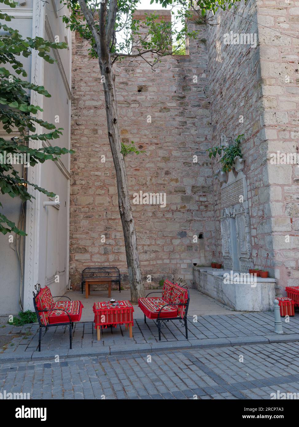 Tavolo e sedie in tessuto rosso pronti per il tè turco da servire, accanto a un castello costruito in pietra come un muro con merlature in cima Foto Stock