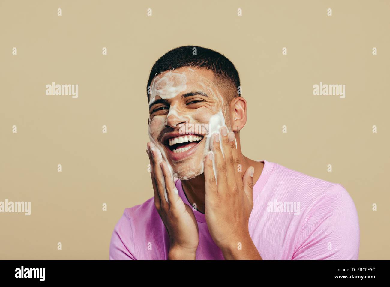 Ritratto di un bel giovane che si prende cura della sua routine di cura e cura di sé mentre applica il lavaggio del viso in uno studio. Uomo giovanile sorridente felicemente whi Foto Stock