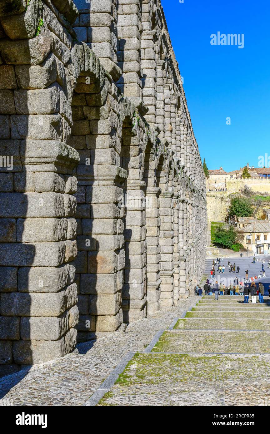 Segovia, Spagna - 11 febbraio 2023: Acquedotto romano. Strada acciottolata e piazza accanto alla struttura dell'acquedotto romano. I turisti o le persone sono nella dista Foto Stock