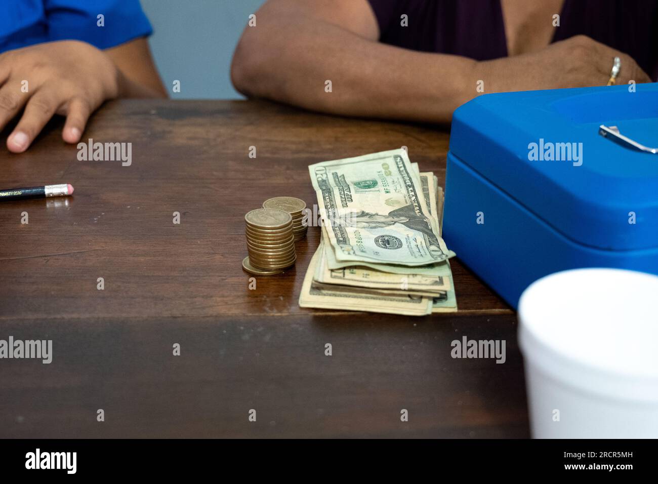 STATI UNITI Dollari e monete accanto a una scatola di metallo blu su un tavolo di legno Foto Stock