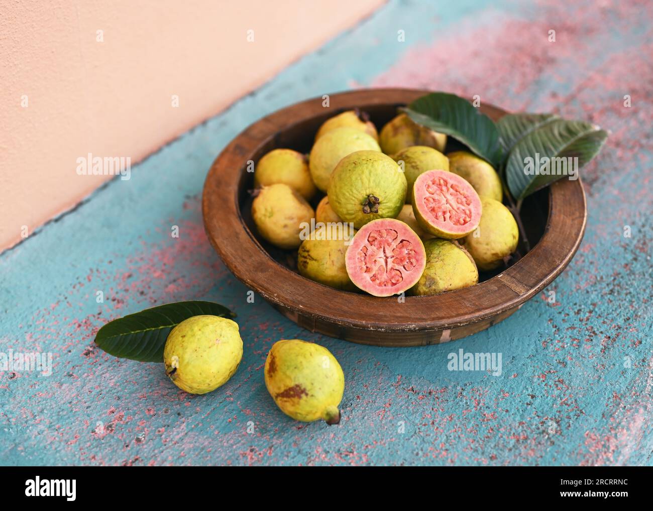 Frutta fresca di guava rosa biologica al palato di legno in giardino. (Psidium guajava) cibo vegano sano o concetto di dieta. Messa a fuoco selettiva. Foto Stock