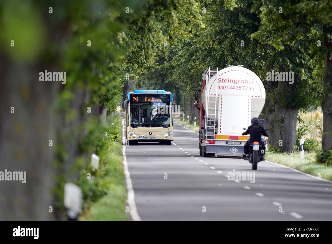 13 luglio 2023, Berlino, Schönefeld: Un autobus della linea 741 con destinazione Rotberg è in auto da Kiekebusch sulla strada di campagna L402 tra avenue Trees. Dall'altro lato della strada, una motocicletta sta guidando dietro un camion. Foto: Soeren Stache/dpa Foto Stock