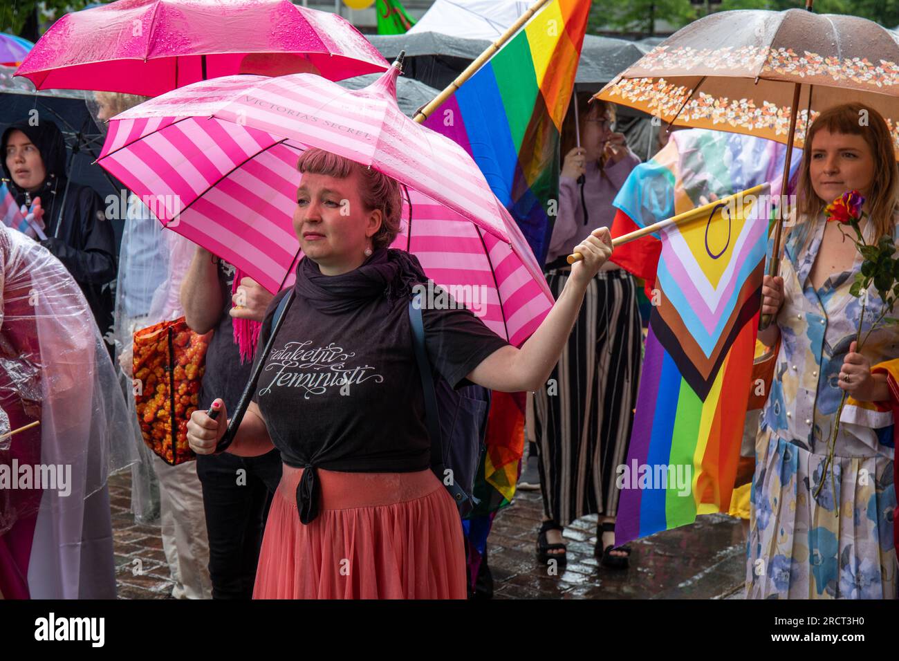 Donna con ombrello rosa che tiene un piatto d'orgoglio alla sfilata Helsinki Pride 2023 in un giorno di pioggia a Helsinki, Finlandia Foto Stock