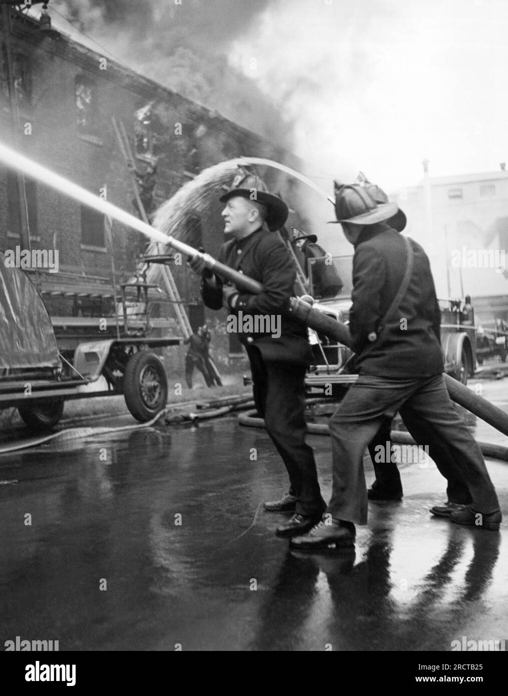 Chicago, Illinois: c. 1935 tre vigili del fuoco dirigono un tubo in un grande edificio in fiamme. Foto Stock