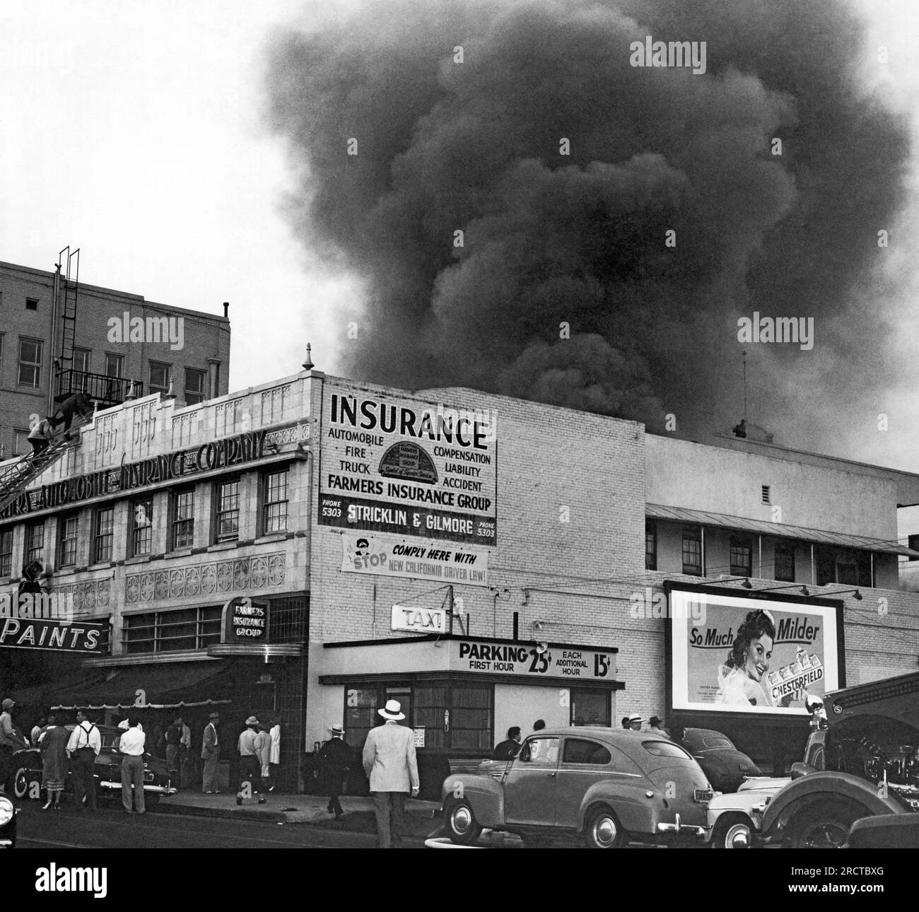 California: 1950 Un Farmers Insurance Building in fiamme con un'enorme nuvola di fumo che esce dal tetto. Foto Stock