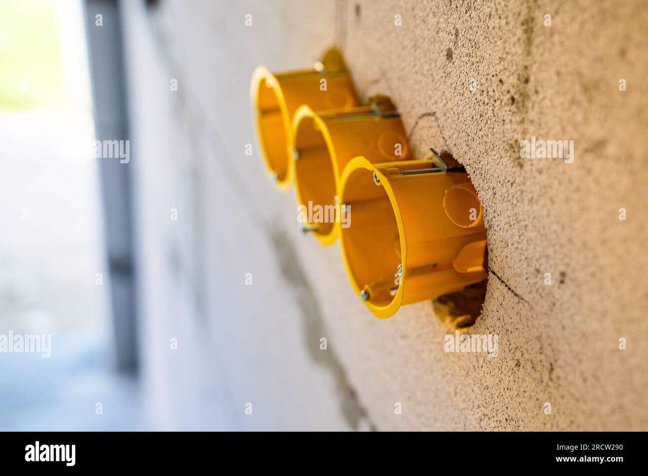 Scatola di installazione tripla gialla per una presa in una parete a blocchi in calcestruzzo cellulare. Installazione di prese euro rotonde durante la riparazione Foto Stock